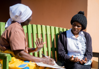 A Friendship Bench Grandmother sitting with her client on simple wooden park bench, using an evidence-based approach to probelm-solving therapy to get people out of depression in Zimbabwe. Credit: The Friendship Bench